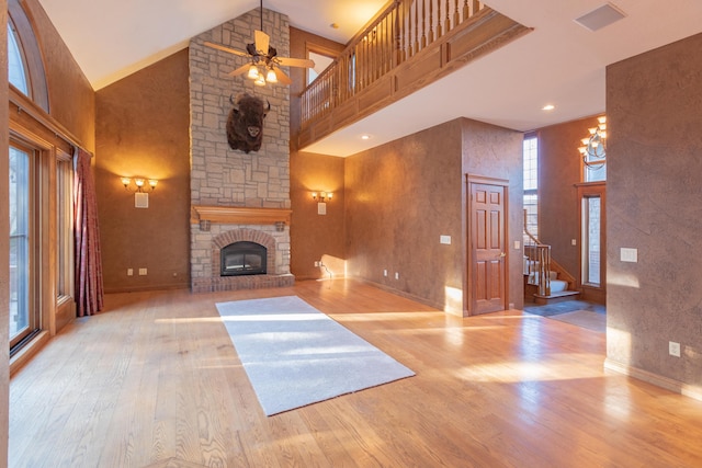 unfurnished living room featuring a stone fireplace, ceiling fan, wood finished floors, and high vaulted ceiling