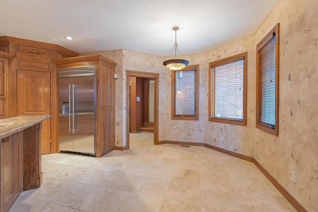 kitchen featuring decorative light fixtures, light stone counters, baseboards, and built in fridge