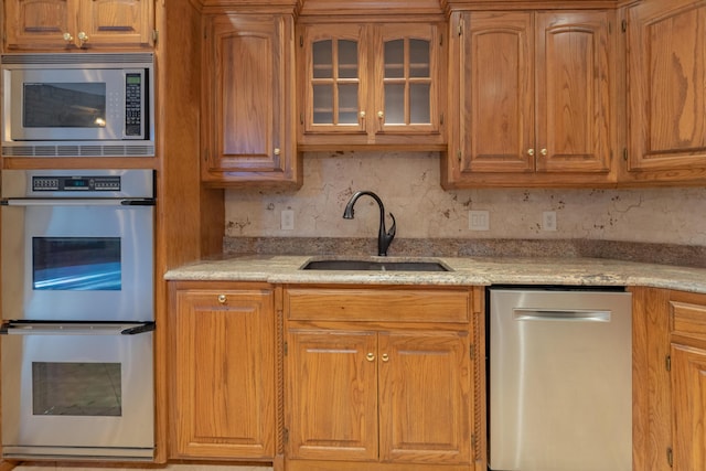 kitchen with decorative backsplash, a sink, stainless steel appliances, glass insert cabinets, and light stone countertops