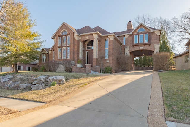 view of front of home featuring a front yard, brick siding, driveway, and a chimney