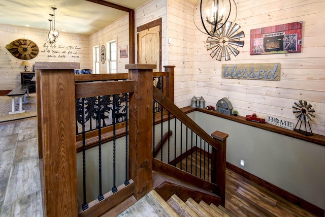 staircase featuring a chandelier, baseboards, wooden walls, and wood finished floors