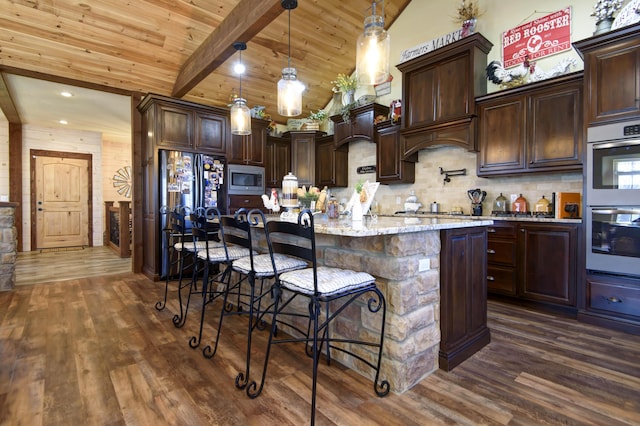 kitchen featuring dark wood finished floors, dark brown cabinetry, appliances with stainless steel finishes, a kitchen bar, and beamed ceiling