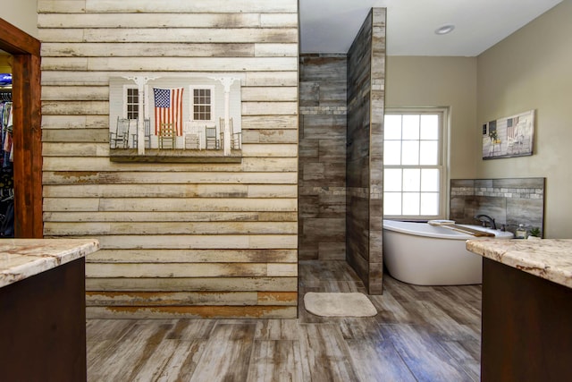 bathroom featuring vanity, wood finished floors, a freestanding bath, a spacious closet, and a tiled fireplace