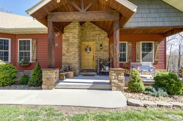 entrance to property featuring stone siding, roof with shingles, and a porch