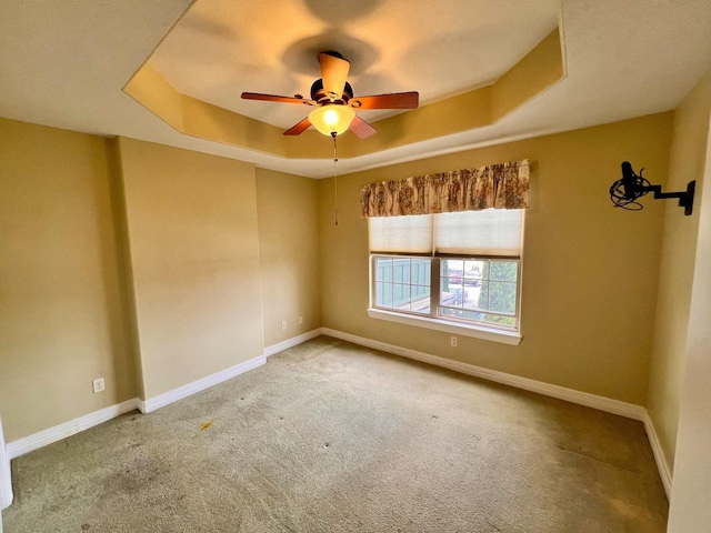 carpeted empty room featuring a tray ceiling, baseboards, and a ceiling fan