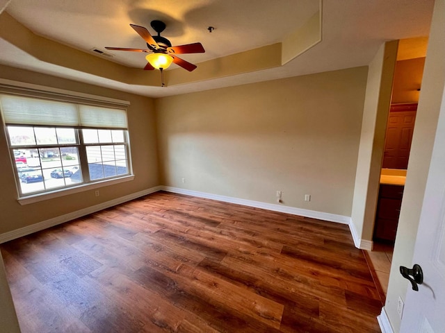 spare room with wood finished floors, visible vents, baseboards, a tray ceiling, and ceiling fan