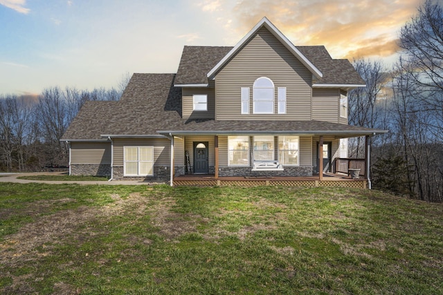 view of front of home featuring stone siding, covered porch, a shingled roof, and a yard