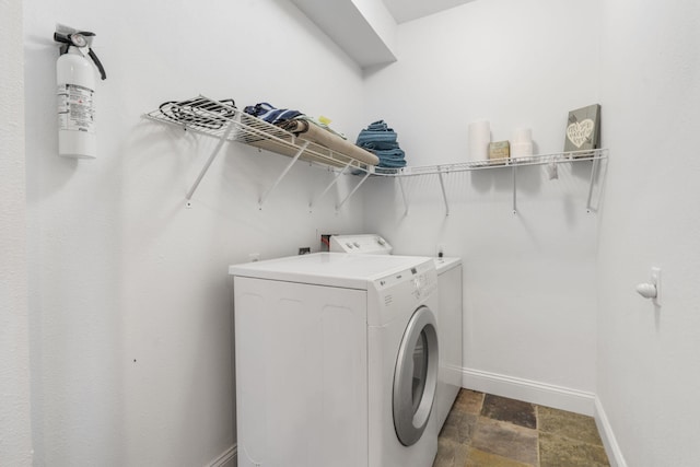 clothes washing area with independent washer and dryer, laundry area, stone finish floor, and baseboards