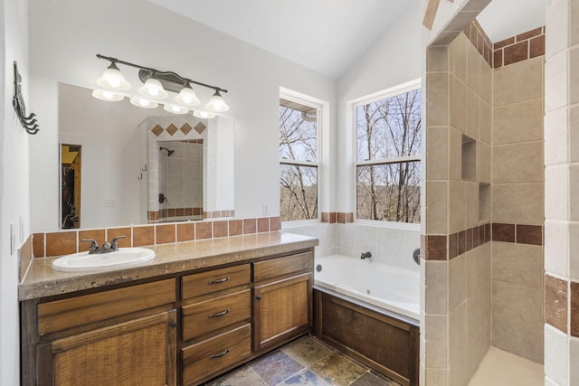 bathroom featuring a garden tub, vaulted ceiling, a tile shower, stone tile flooring, and vanity