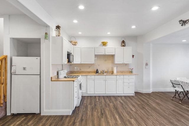 kitchen with a sink, white appliances, dark wood-type flooring, and white cabinets