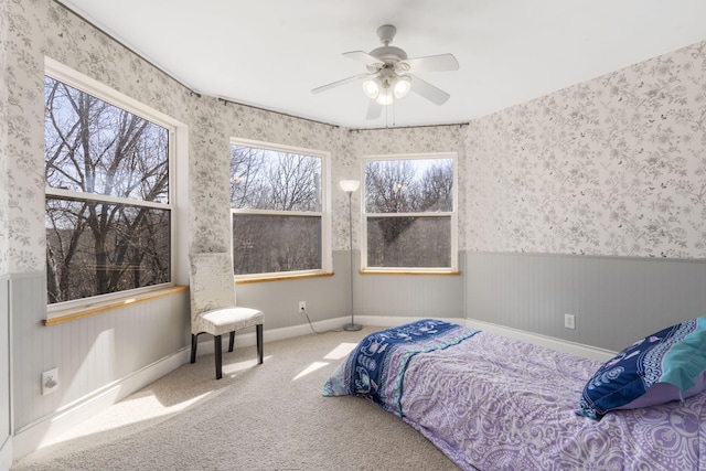 bedroom with wallpapered walls, carpet flooring, a ceiling fan, and a wainscoted wall