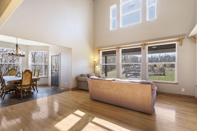 living room featuring baseboards, wood-type flooring, a high ceiling, and an inviting chandelier