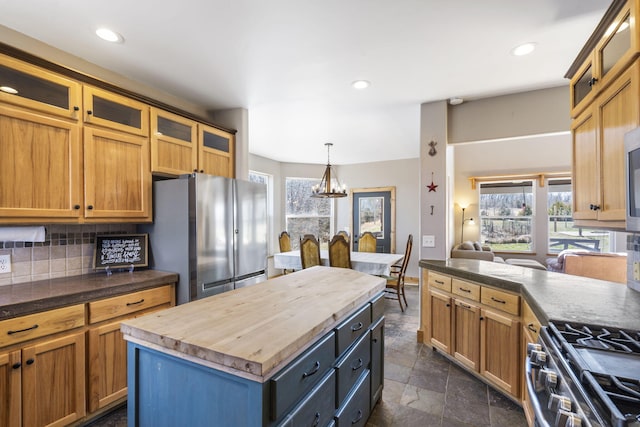 kitchen with butcher block countertops, decorative backsplash, stone tile flooring, appliances with stainless steel finishes, and a notable chandelier