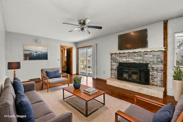 living area with a fireplace, wood finished floors, a baseboard heating unit, and a ceiling fan