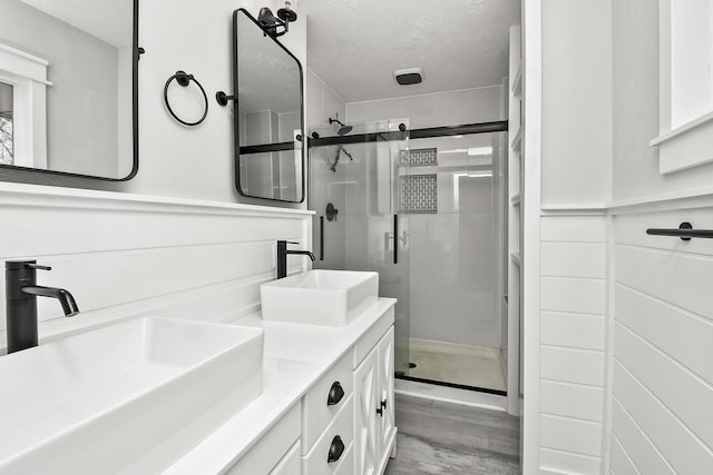 full bath featuring a sink, wood finished floors, a textured ceiling, and a stall shower