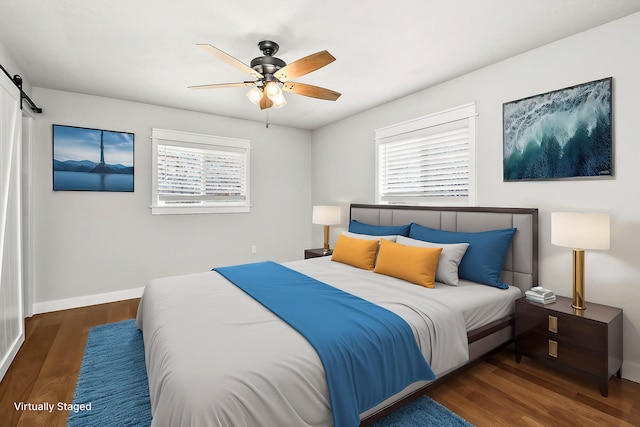 bedroom with a ceiling fan, a barn door, wood finished floors, and baseboards