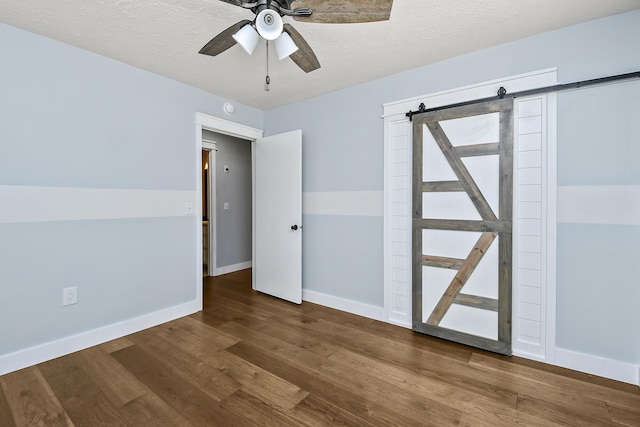 unfurnished room with baseboards, a ceiling fan, a barn door, and wood finished floors