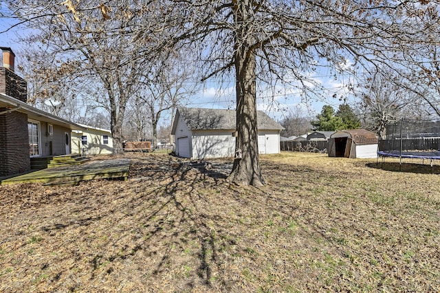 view of yard with a storage unit, a trampoline, fence, an outdoor structure, and a garage