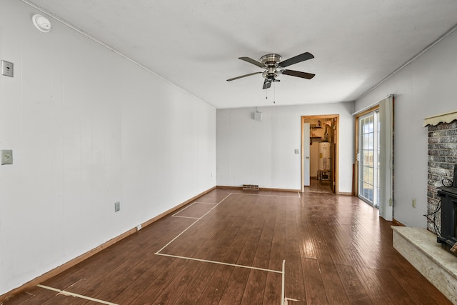 unfurnished living room featuring hardwood / wood-style floors, a wood stove, baseboards, and ceiling fan