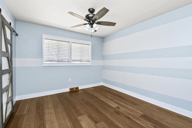 spare room featuring visible vents, ceiling fan, baseboards, dark wood finished floors, and a barn door