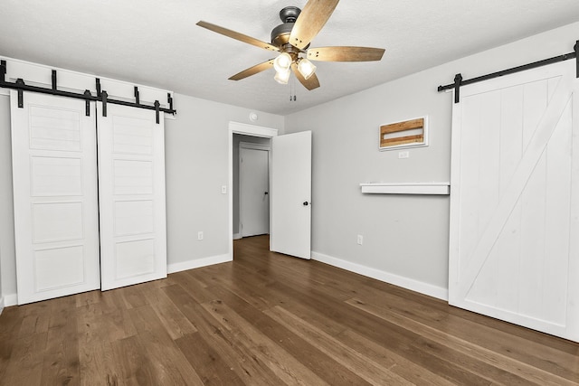 unfurnished bedroom featuring a barn door, baseboards, a textured ceiling, and wood finished floors