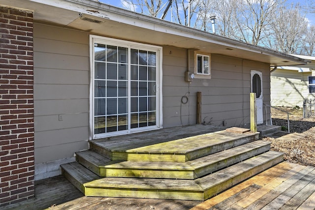 view of exterior entry featuring brick siding and a wooden deck