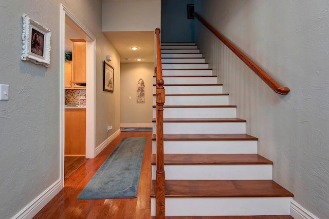 stairs featuring baseboards, wood finished floors, and a textured wall