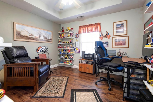 office space with visible vents, a ceiling fan, wood finished floors, baseboards, and a raised ceiling