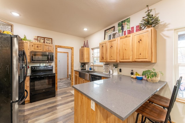 kitchen with stainless steel microwave, a peninsula, freestanding refrigerator, black electric range, and a sink