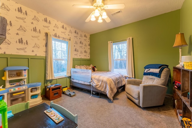 bedroom featuring wallpapered walls, ceiling fan, carpet, and wainscoting