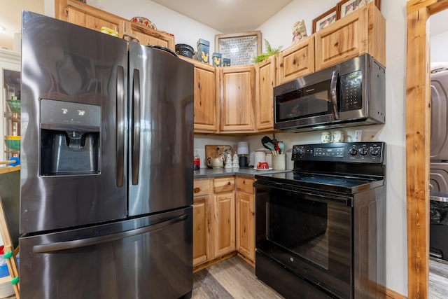 kitchen featuring stainless steel appliances, stacked washer and dryer, dark countertops, and light wood-style flooring