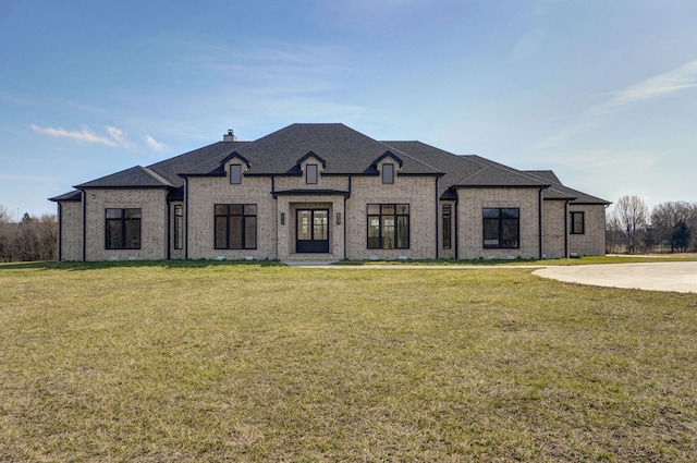 french country home with brick siding, a chimney, a front lawn, and a shingled roof