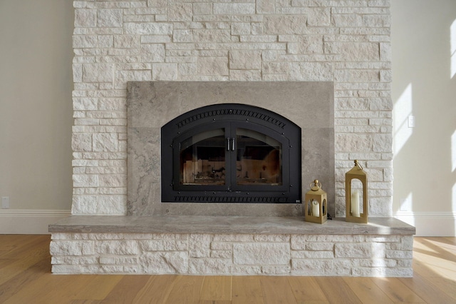 room details featuring baseboards, a stone fireplace, and wood finished floors