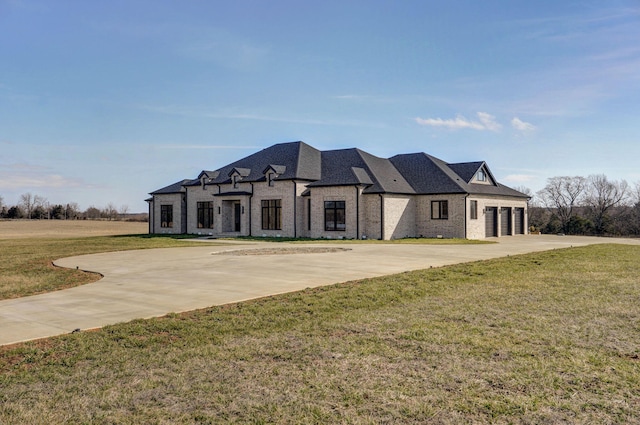 french country inspired facade with an attached garage, concrete driveway, a front yard, and roof with shingles