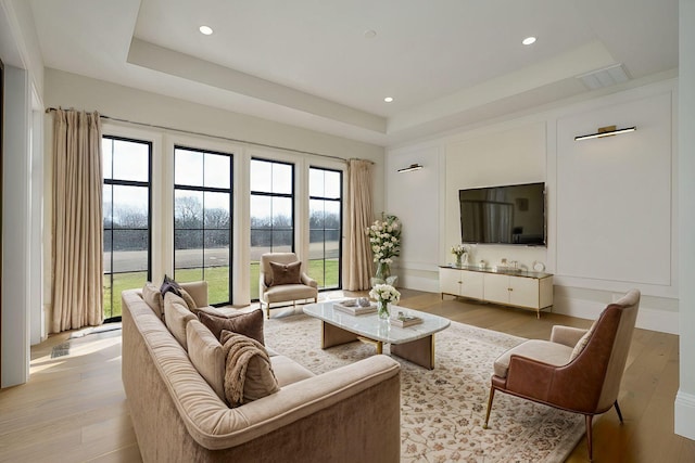 living room with a raised ceiling, recessed lighting, light wood-type flooring, and visible vents