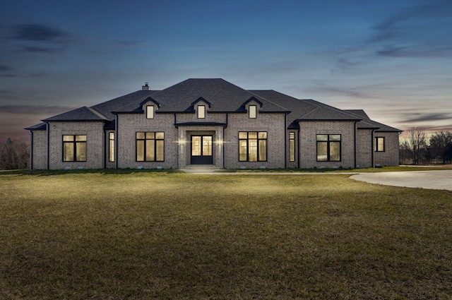 french country style house featuring brick siding, a chimney, a front lawn, and a shingled roof