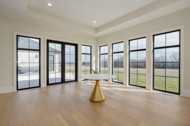 interior space featuring a raised ceiling, light wood-style flooring, french doors, and visible vents