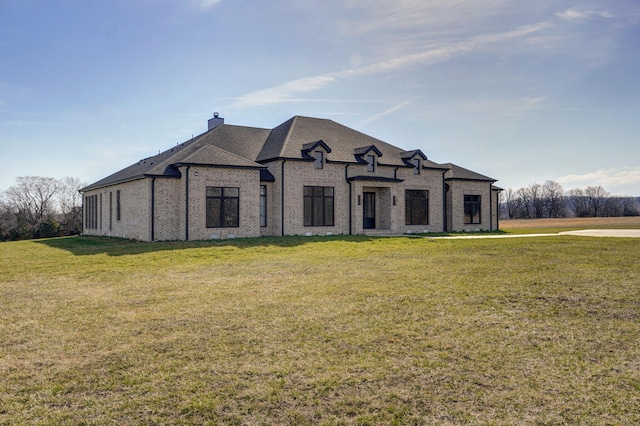 french country style house with brick siding, a chimney, a front yard, and a shingled roof