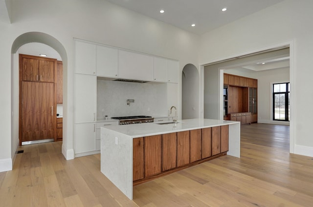 kitchen featuring light wood finished floors, arched walkways, a sink, decorative backsplash, and light countertops