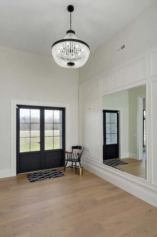 foyer entrance with visible vents, light wood-style flooring, french doors, a towering ceiling, and a decorative wall