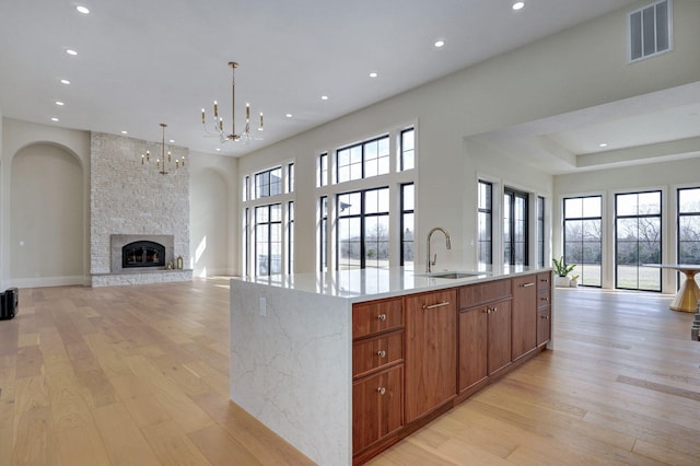 kitchen featuring visible vents, a kitchen island with sink, light wood-style flooring, a sink, and open floor plan