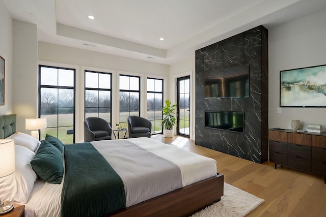 bedroom featuring a high end fireplace, visible vents, a tray ceiling, recessed lighting, and light wood-style floors