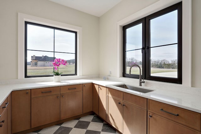 kitchen featuring light stone counters, light floors, brown cabinets, and a sink