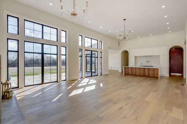 unfurnished living room with an inviting chandelier, light wood-style flooring, recessed lighting, and arched walkways