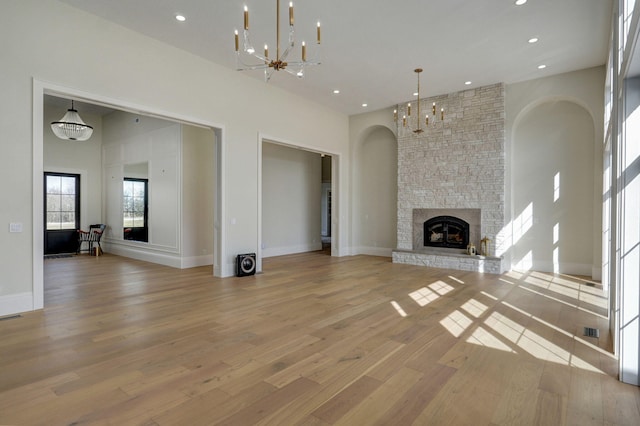 unfurnished living room with light wood finished floors, a stone fireplace, recessed lighting, a towering ceiling, and a notable chandelier