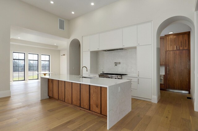 kitchen with a sink, arched walkways, tasteful backsplash, and light wood-style flooring