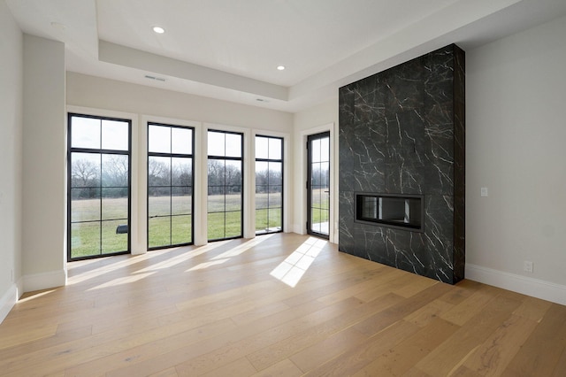 unfurnished living room with baseboards, a premium fireplace, recessed lighting, light wood-style flooring, and a raised ceiling