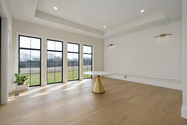 spare room with a decorative wall, recessed lighting, light wood-style floors, and a tray ceiling