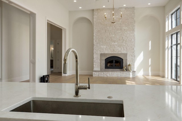 room details with wood finished floors, light stone countertops, recessed lighting, a sink, and a stone fireplace