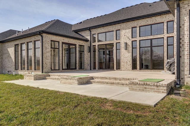 rear view of property featuring brick siding, a hot tub, roof with shingles, and a patio area